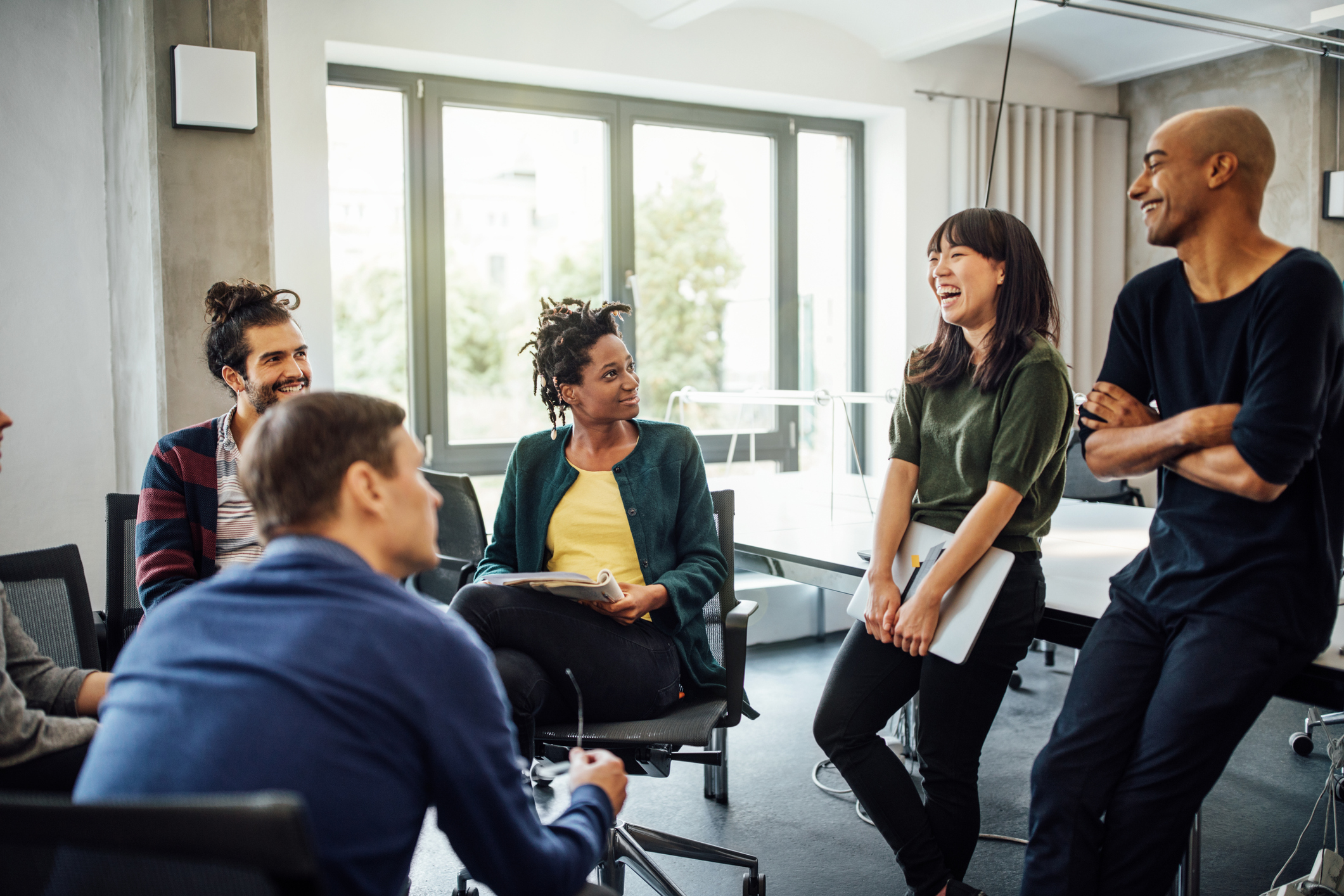 A group of diverse people in an office setting talking and smiling.