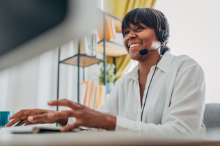 Woman with headset smiling typing on a computer.