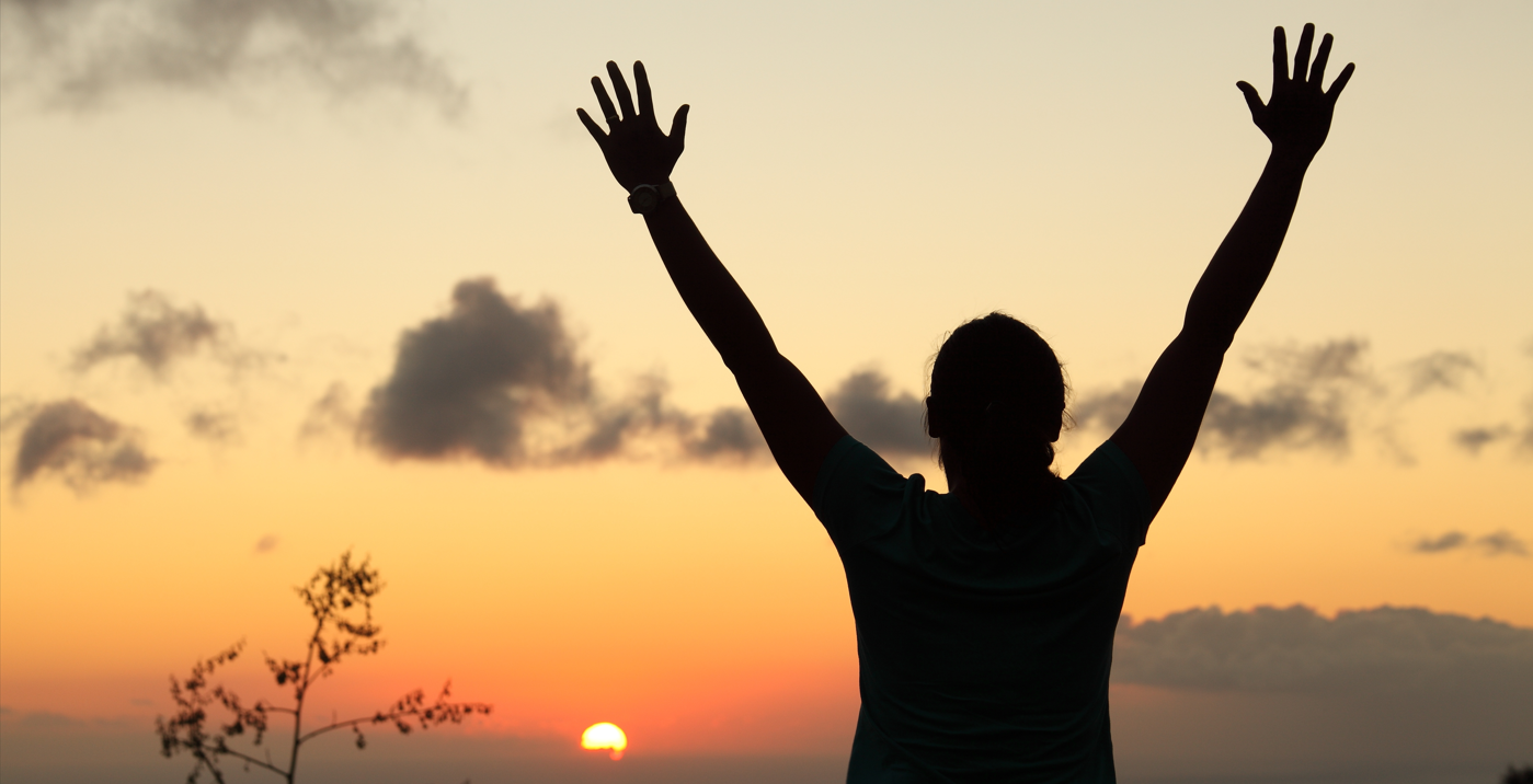 Person viewing sunset with arms in the air.